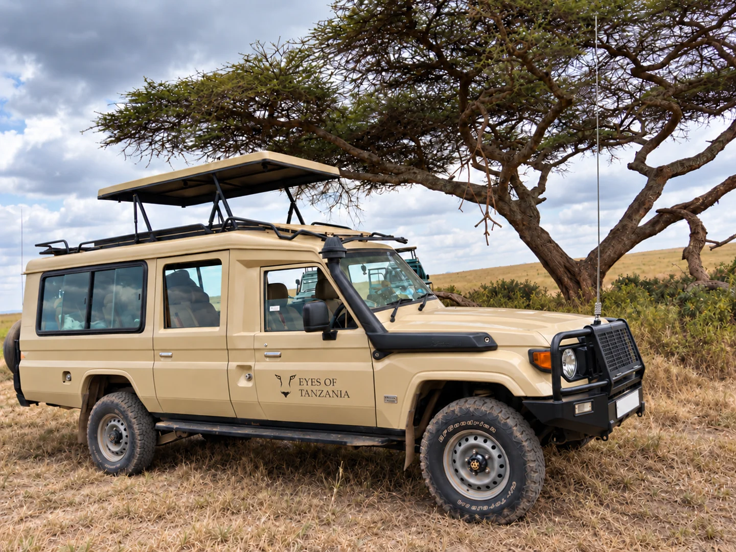 Eyes of Tanzania safari Land Cruiser with its pop-up roof raised beneath an acacia tree